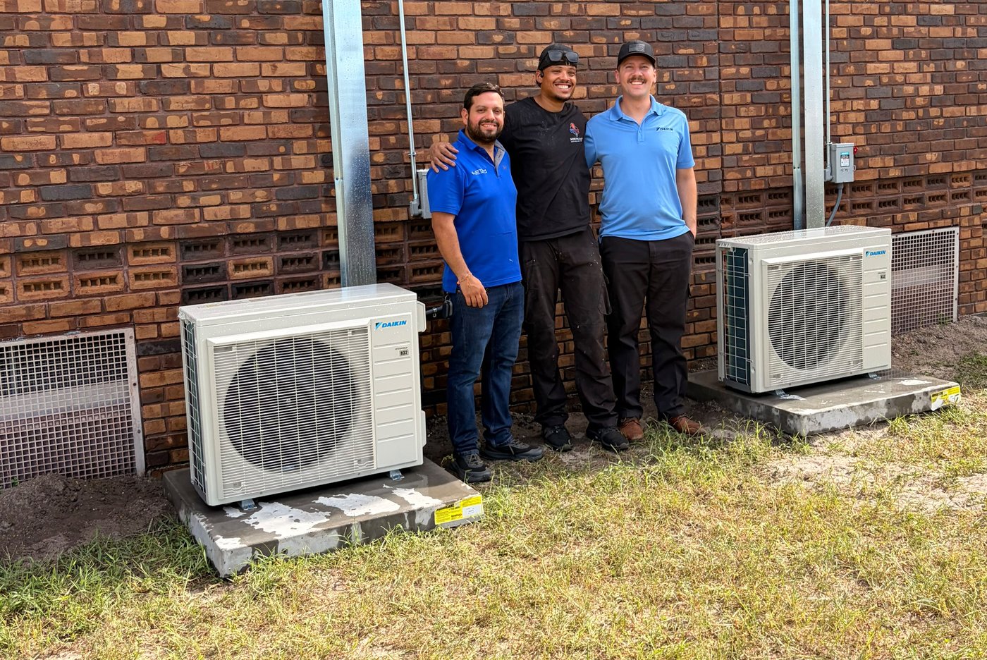Chris Grullon of North East Heating And Cooling with the Daikin representative and the electrician from Atom, standing between two new Daikin mini-split condensers